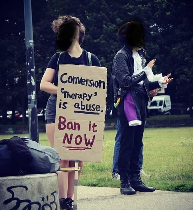 A protestor holding a sign that reads 'Conversion "therapy" is abuse. Ban it NOW.'