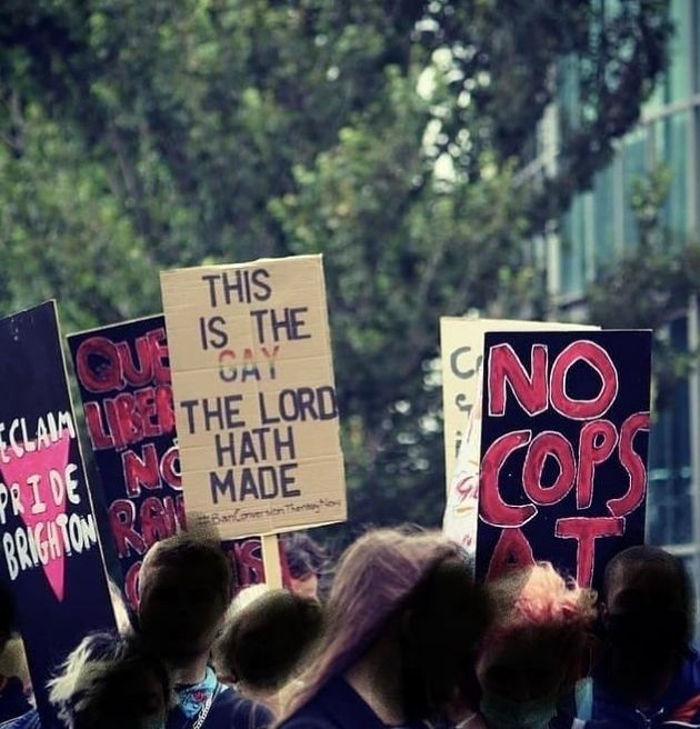 A crowd holds a variety of placards. The placard at the centre of the image reads: 'This is the gay the lord hath made'