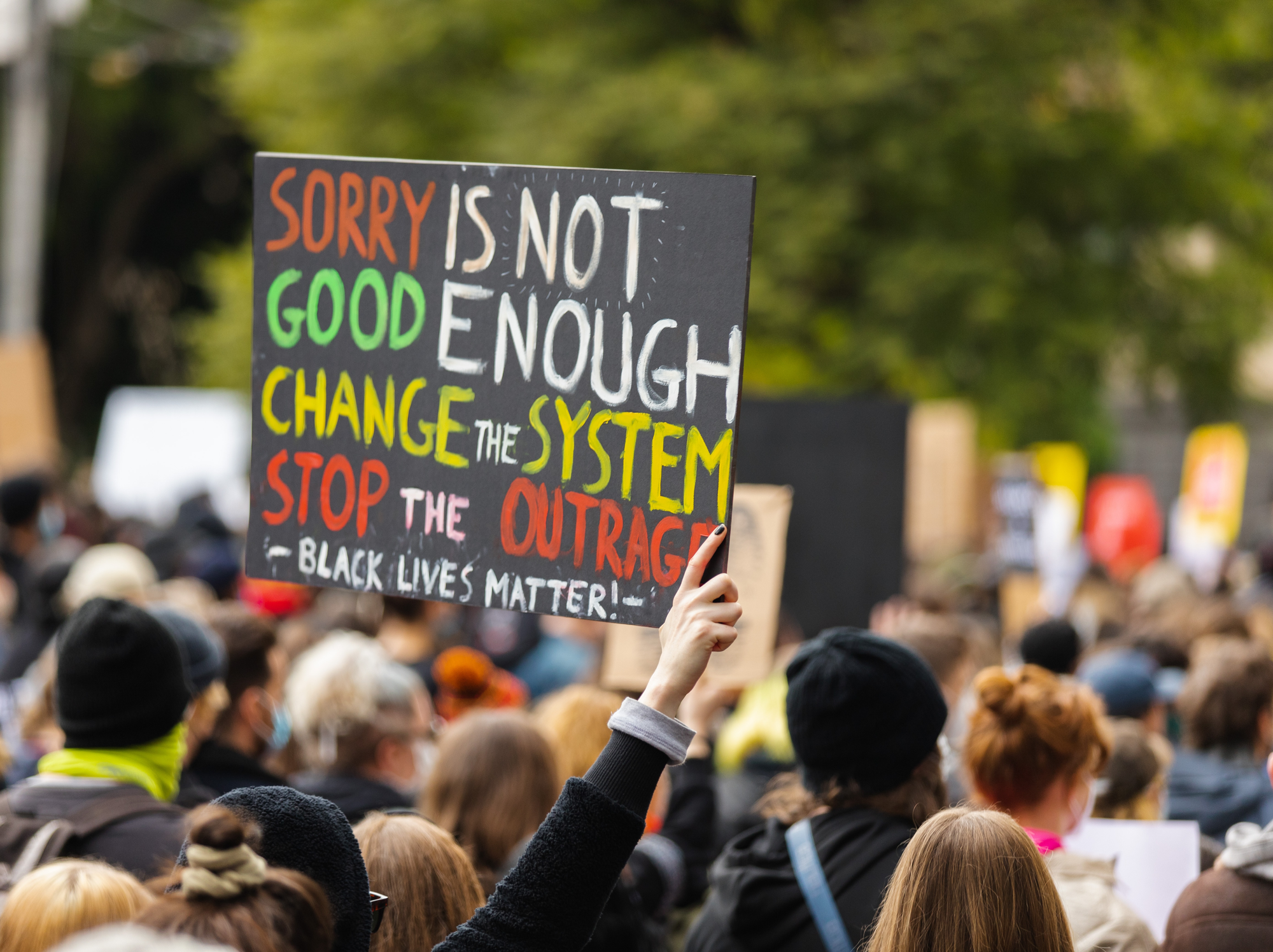 At a Black Lives Matter protest, somebody holds up a placard that reads, 'Sorry is not good enough, change the system, stop the outrage.'