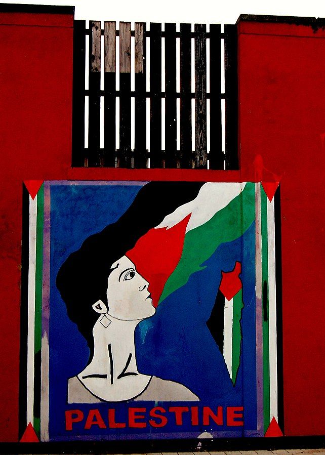 A mural on a wall depicting a person whose hair extends upwards into the image of a Palestinian flag. Below them is the word 'Palestine'. To their right is the map outline of Israel, Gaza, and the West Bank, all encompassed by a Palestine flag.